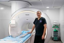 male in scrubs standing beside a MRI scanner