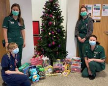 Toy donation, staff beside and kneeling beside a decorated christmas tree with toys